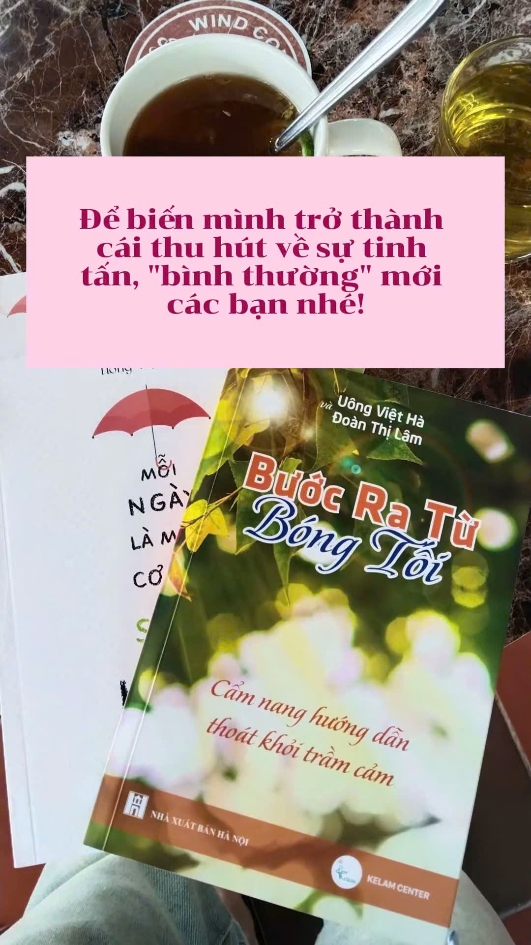 Sách Bước Ra Từ Bóng Tối đặt cạnh ly nước ấm, giúp nuôi dưỡng sự tinh tấn và bình thường mới.